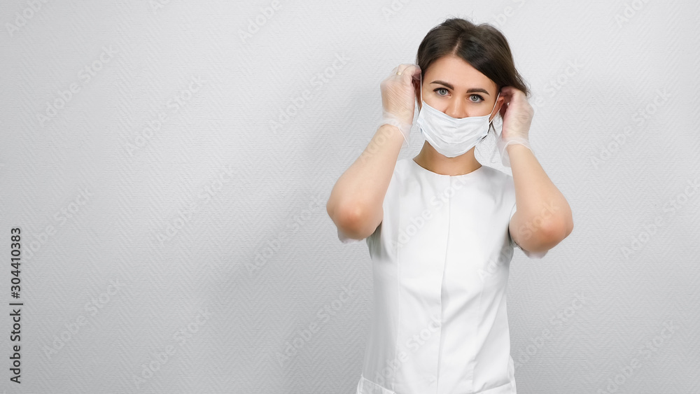 beautiful woman beautician puts on white protection mask standing against medical center wall close view beautiful woman beautician puts on white protection mask standing against medical center wall close view