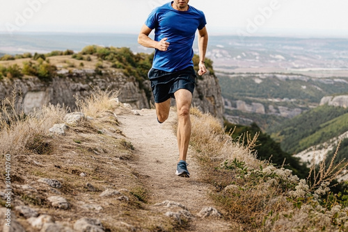 Tela male runner running mountain trail on edge of cliff