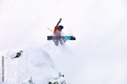 elite snowboarder frozen at the moment of the jump. girl Freerider jumping off a cliff in a remote taiga in a snowstorm. poor visibility and Heli skiing