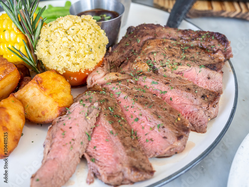 Ribeye beef steak medium to well done grilled served with corn, pototoes and asparagus in restaurant photo