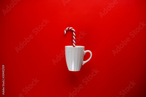 White ceramic cup with Christmas candy on a red background. Flat lay.