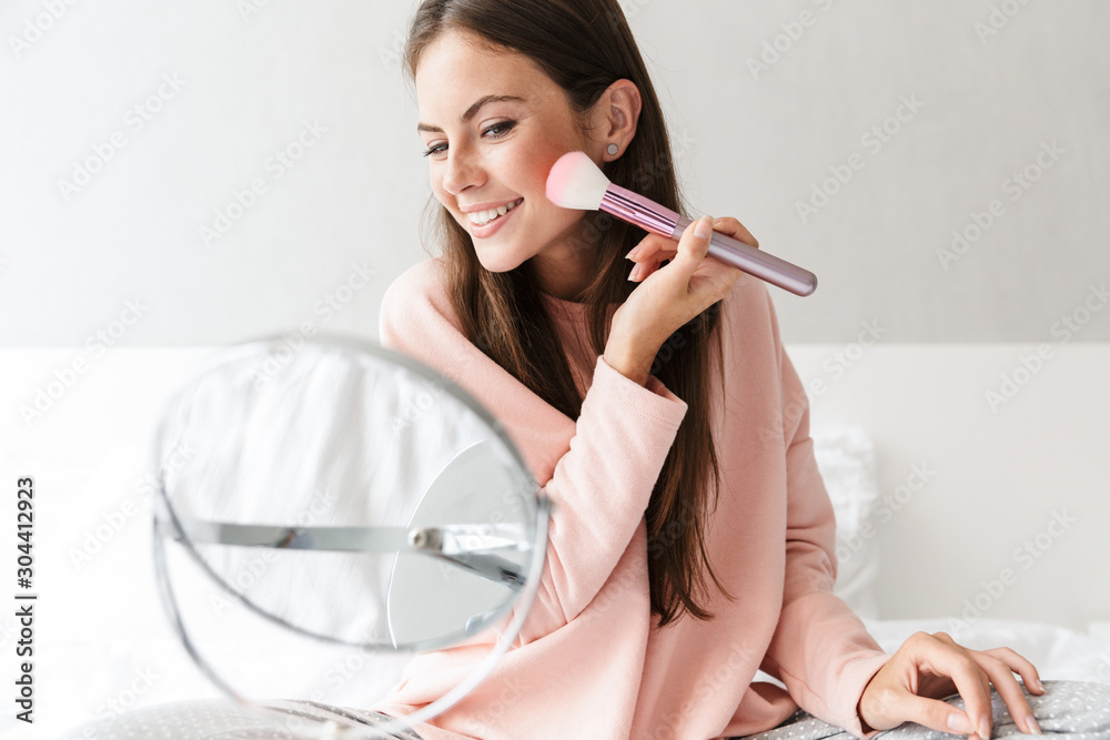 Smiling lovely girl wearing pajamas applying makeup Smiling lovely girl wearing pajamas applying makeup