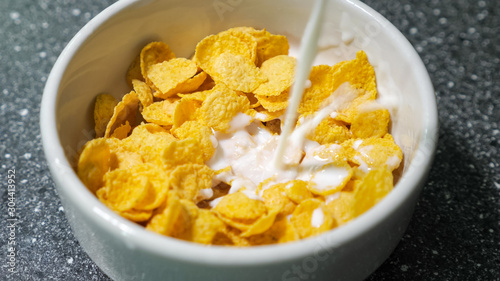 Preparing fast breakfast with cereal. Pouring milk in bowl with dry cornflakes. Traditional morning food.