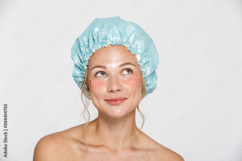 Image of woman wearing cosmetic patches and shower cap looking upward - obrazy, fototapety, plakaty 