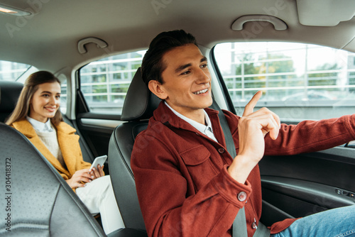 Smiling taxi driver and passenger with smartphone in car
