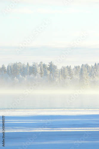 Finnish winter. Crystal clear cold winter day. Lake Porontima, Kuusamo. Bright colors and snowy forest on backround.Mist on the lake and pastel color cloudletts.