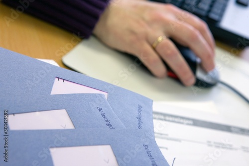 Hand with mouse and computer. Dutch tax papers. Belastingdienst. Blue enveloppe. tax assessment. Administration. Bookkeeping. Belastingformulier invullen. photo