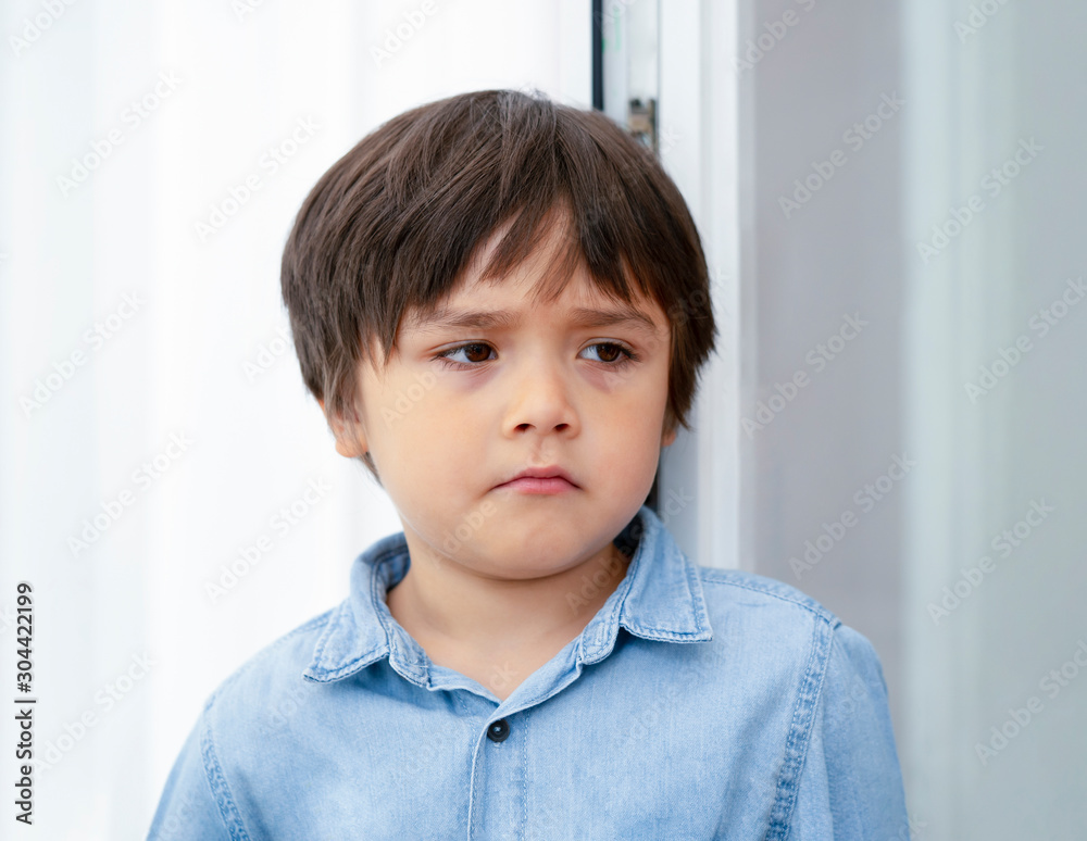 Portrait of Sad boy wearing standing next to the glass door with upset face ,Lonely child boy ith bored face, Dramatic portrait of Toddler on corner punishment,Spoiled children concept Portrait of Sad boy wearing standing next to the glass door with upset face ,Lonely child boy ith bored face, Dramatic portrait of Toddler on corner punishment,Spoiled children concept