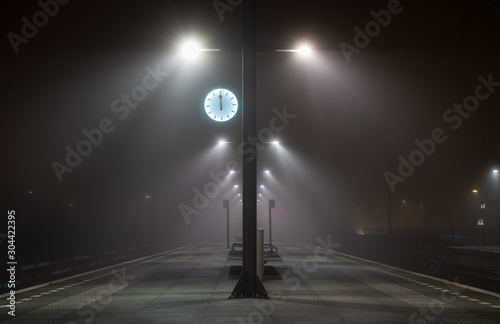 Illuminated, empty platform at a railroad station during a foggy night in autumn.