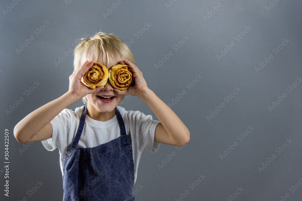 The child amusedly closed his eyes with Cinnabons. The boy seemed to look through the buns into the distance, like a little explorer. On the right, where the gaze is directed, there is a copyspace.