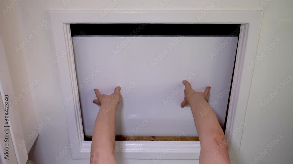 Slow motion close POV shot of a man’s hands reaching up and sliding open the hatch door to the loft space of his home. Slow motion close POV shot of a man’s hands reaching up and sliding open the hatch door to the loft space of his home.