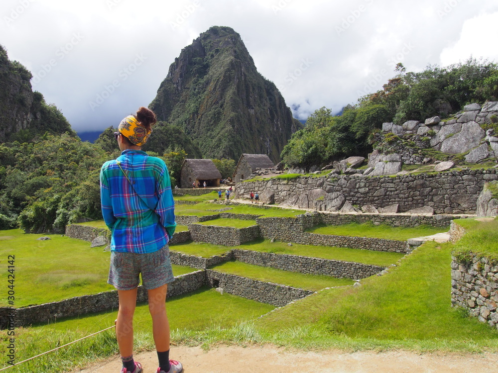 A woman tourist standing in the ancient Inca town of Machu Picchu with Huayna Picchu Mountain in the background, Ruins of Inca Empire city, Peru