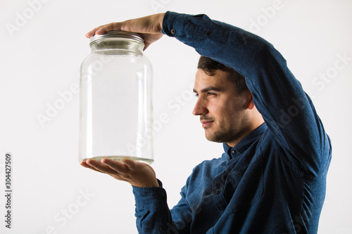 Close up profile portrait of a curious businessman holding an empty glass jar in his hands looking with sneaky eyes isolated over white background. photo