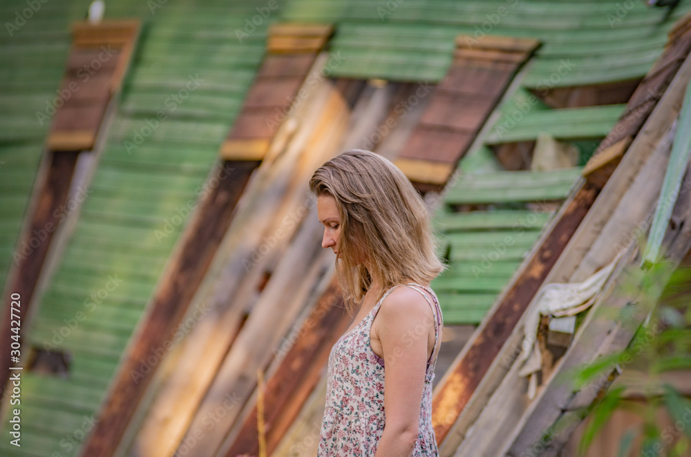 A woman in a dress stands in the background of an old abandoned dilapidated house A woman in a dress stands in the background of an old abandoned dilapidated house