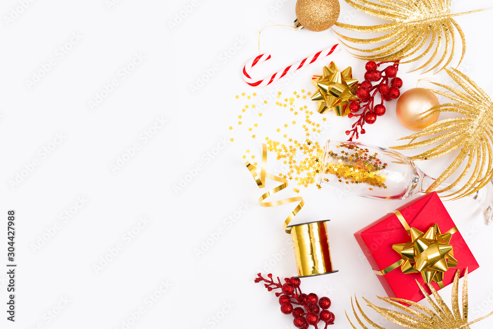 Glass of champagne with glitter and holiday decorations and gift box on a white background, top view. New Year or Christmas