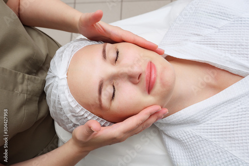 masseuse hands move slowly doing calming face massage to beautiful girl client in medical center top view