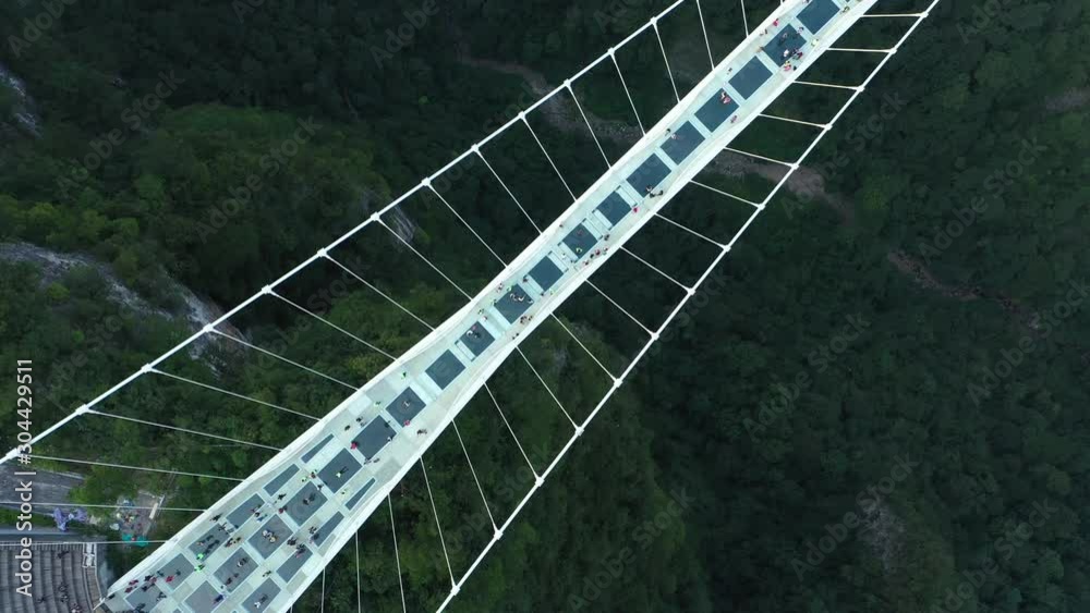 Bird's eye perspective of people walking across glass bridge over mountain valley in famous Zhangjiajie 'avatar' national park in China
