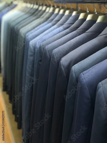 A row of men's suits, jackets hanging on a rack for display.