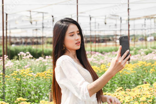 Young beautiful asian woman taking selfie by smartphone in chrysanthemum garden