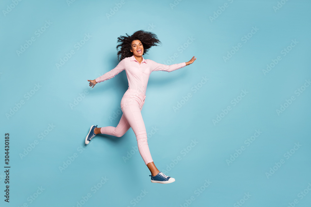 Full length photo of amazing dark skin lady jumping high spread hands sides spending best free time outside wear pink shirt trousers isolated blue color background