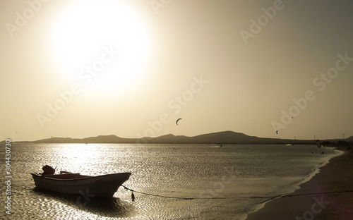 Golden beach landscape at golden light sunset, with boat on the shore, calm sea and mountains in the background,