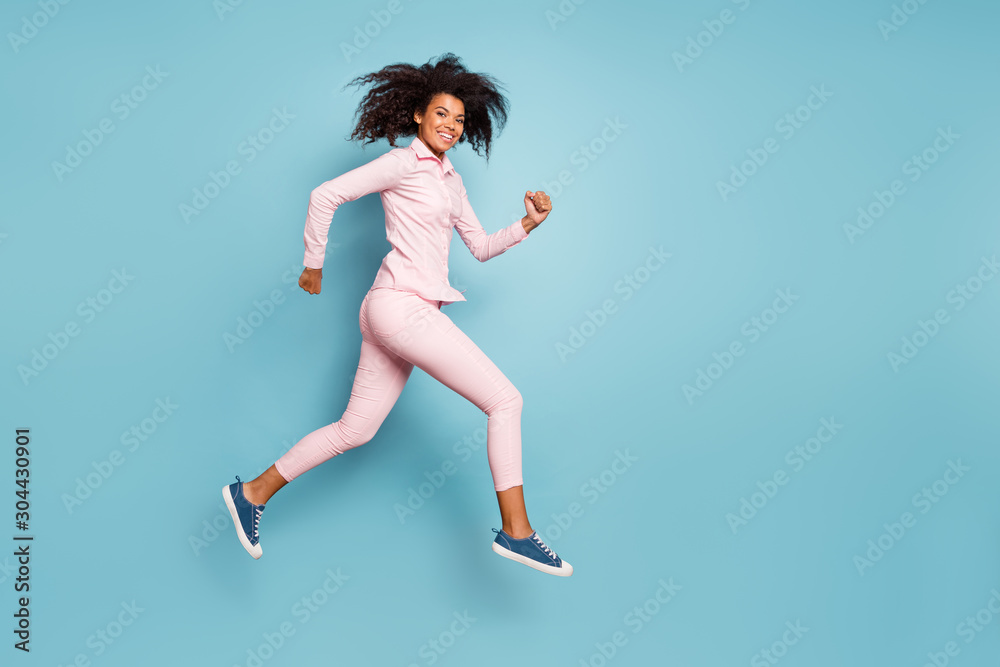 Full length photo of amazing dark skin wavy lady jumping high speed race competition participant wear pink shirt trousers isolated blue color background