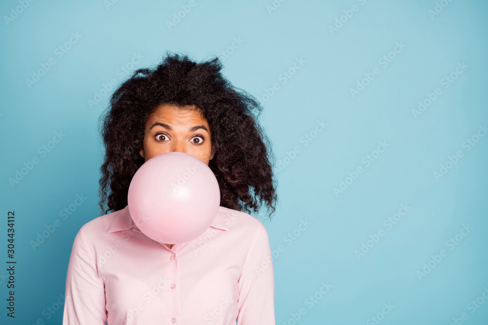 Closeup photo of pretty wavy dark skin lady holding big air balloon in mouth closing half crazy facial expression blowing wear pink shirt isolated blue color background Closeup photo of pretty wavy dark skin lady holding big air balloon in mouth closing half crazy facial expression blowing wear pink shirt isolated blue color background
