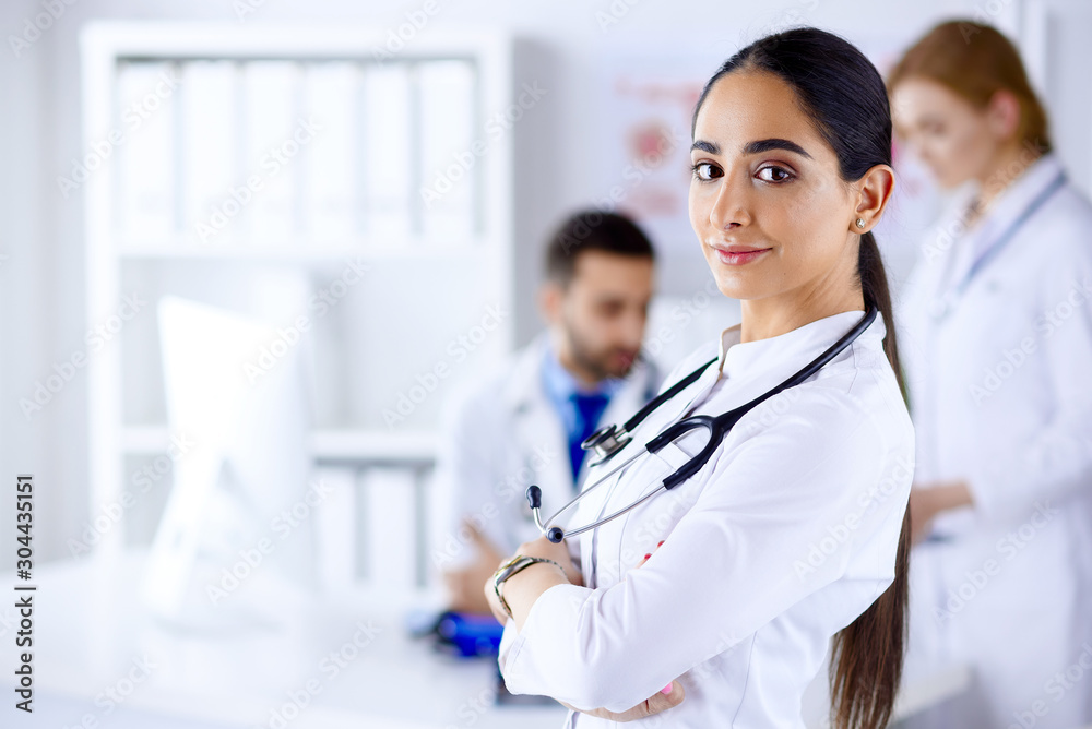 Confident female doctor in front of team, looking at camera smiling, multiracial team with arab female doctor Confident female doctor in front of team, looking at camera smiling, multiracial team with arab female doctor