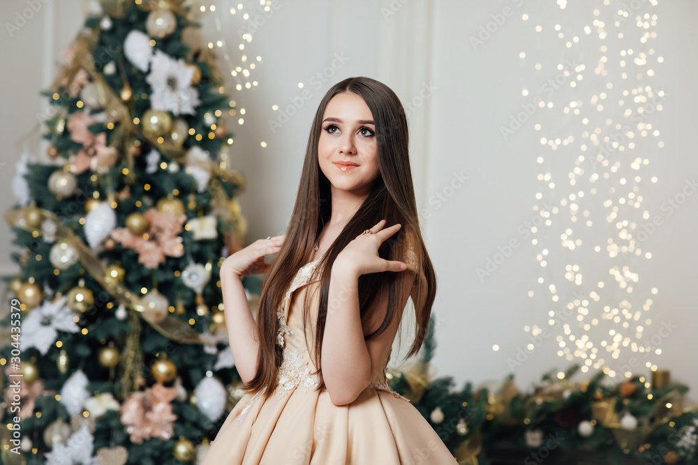 Fashion portrait of girl indoors with Christmas tree.  Girl with make up and hairstyle.  New year concept. Happy young girl ready for celebration at New Year eve. Feast of Christmas. 