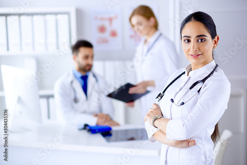 Confident female doctor in front of team, looking at camera smiling, multiracial team with arab female doctor