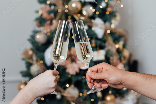 Glasses of champagne on the background of Christmas tree lights. New Year eve. Feast of Christmas. Loving couple banging champagne glasses on New Year\'s night
