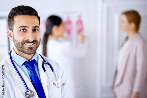 Arab doctor in the office with tablet and stethoscope, nurse working with patient on the background