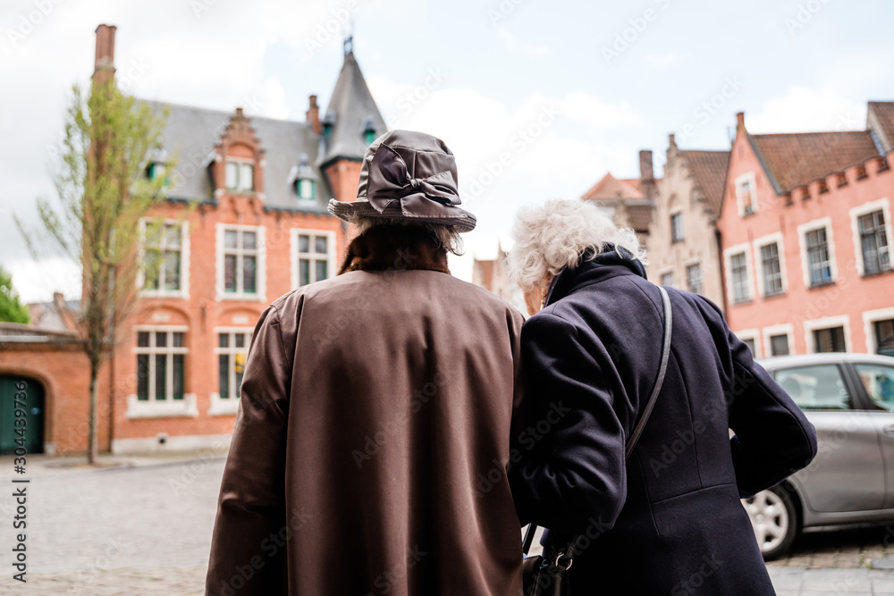 Two elegant elderly ladies walk together in an old city, view from the back. The concept of mutual support of the elderly, sorrow, mutual assistance, friendship of the elderly, spending leisure time.