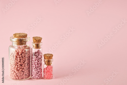 Fotografie, Obraz Beige, purple, orange and yellow beads in glass jars on a bright pink background