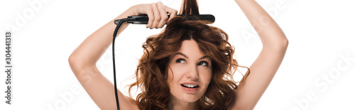 panoramic shot of curly woman using hair straightener isolated on white