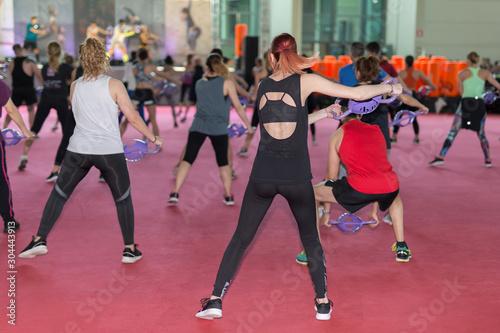 Girls Exercising with Gym double handle Dumbbell in Fitness Class at Gym with Music and Teacher on Stage