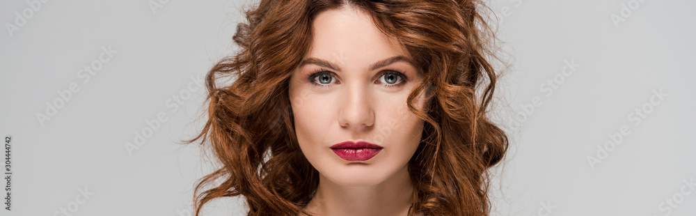 panoramic shot of attractive and curly woman looking at camera isolated on grey panoramic shot of attractive and curly woman looking at camera isolated on grey