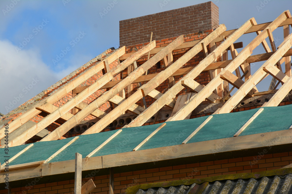 Obraz premium House rooftop wooden frame construction. Incomplete house rooftop roofing construction trusses, vapor barrier, wooden beams, eaves, timber.