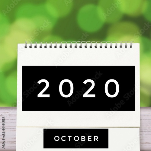 White blank paper desk spiral October calendar on wood with green abstract background. Calender of 2020 and empty month or Date to enter text and numbers.