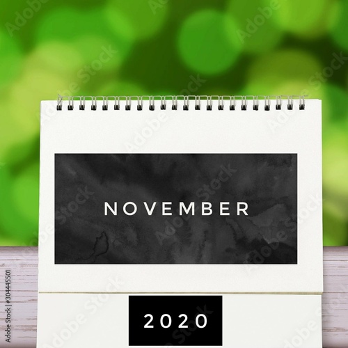 White blank paper desk spiral November calendar on wood with green abstract background. Calender of 2020 and empty month or Date to enter text and numbers.