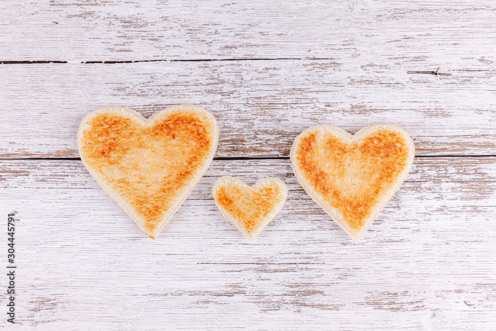 Obraz premium Toasted bread hearts together on white wooden table background. Concept of support in happy family.