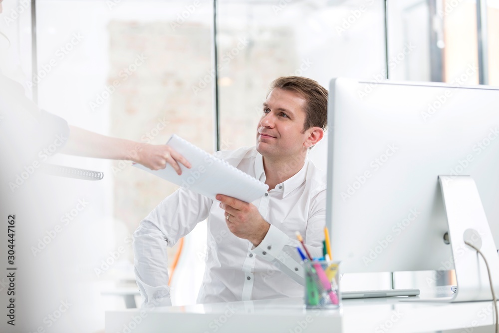 Secretary giving and showing file to manager in office