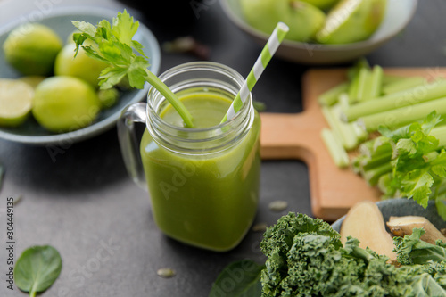 healthy eating, food and vegetarian diet concept - close up of glass mug of fresh green juice or smoothie with paper straw, fruits and vegetables on slate stone background photo
