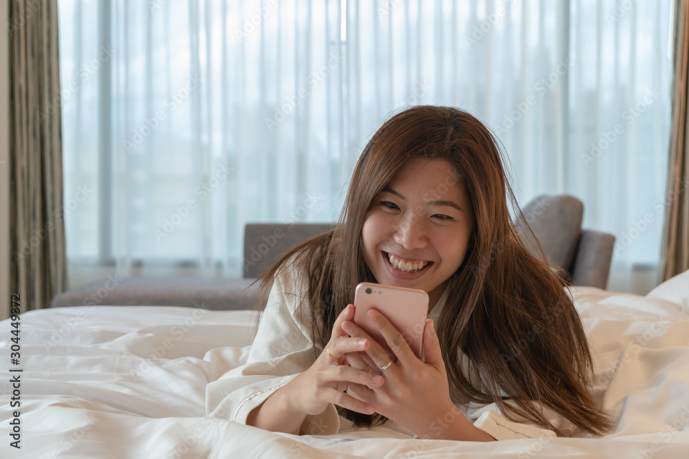 Asian woman in bathrobe suit using smartphone with feeling happy on a bed Asian woman in bathrobe suit using smartphone with feeling happy on a bed