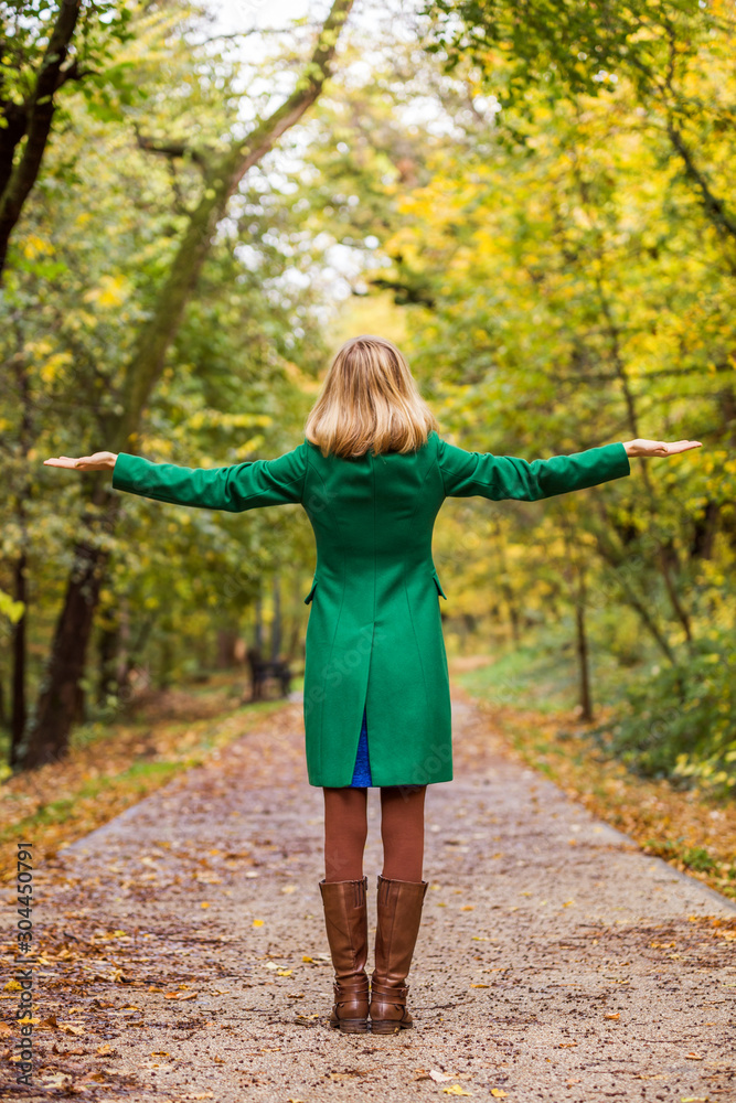 Woman with her arms outstretched enjoys in autumn while standing in the park.	