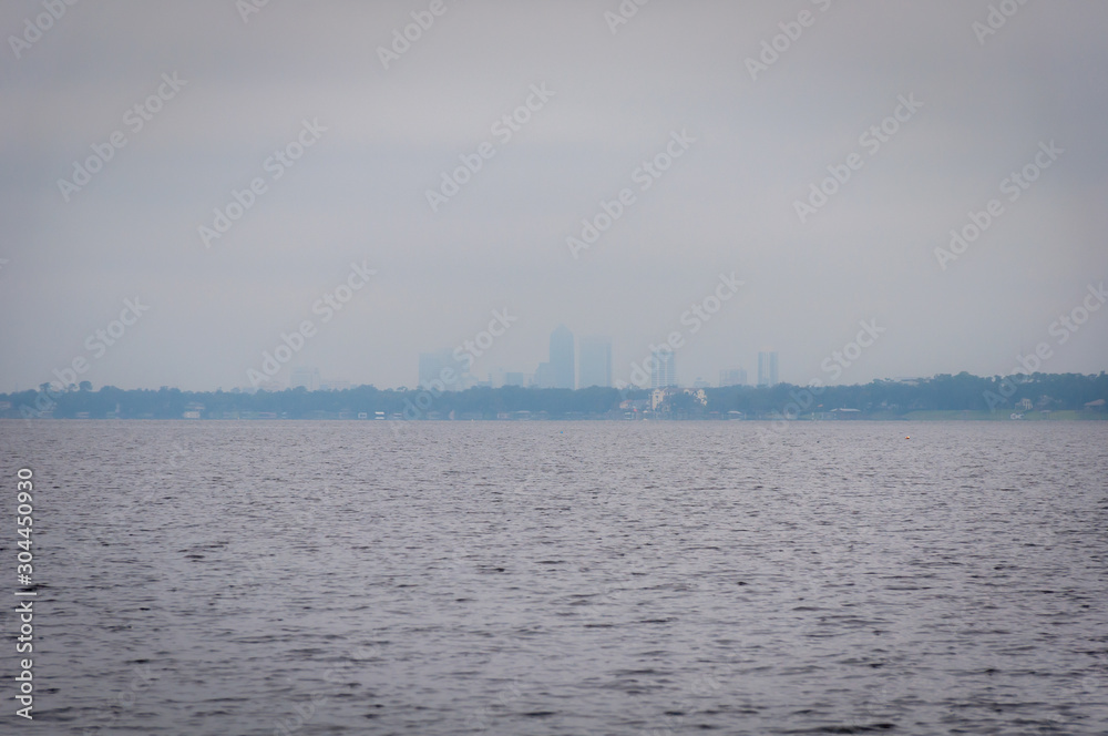 Downtown Jacksonville skyline viewed over St. Johns River from a long distance and threw the morning fog, on an overcast and rainy day. Downtown Jacksonville skyline viewed over St. Johns River from a long distance and threw the morning fog, on an overcast and rainy day.