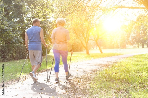 Rear view of senior couple with hiking poles walking in park