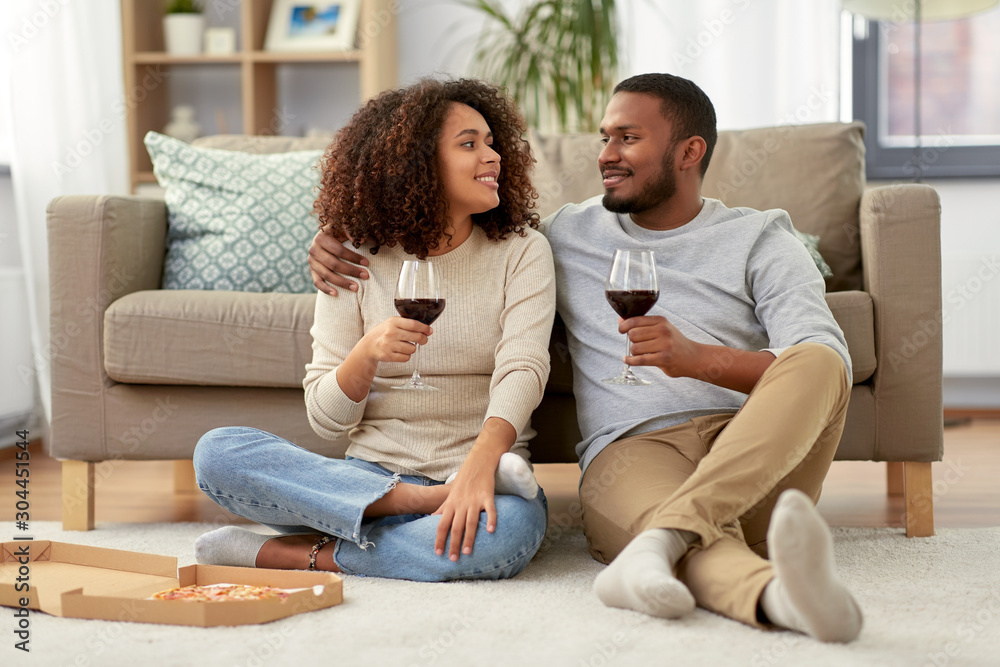 leisure, people and valentines day concept - happy african american couple with wine and takeaway pizza at home