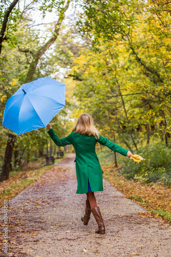 Woman holding umbrella and fall leafs while walking in the park. 