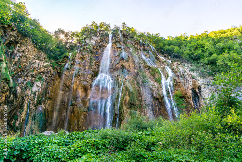Waterfall and blue crystalline water in Plitvice Nation Park (Croatia) in a sunny day in summer during vacations immersed in wild nature with rocks trees flowers and forests